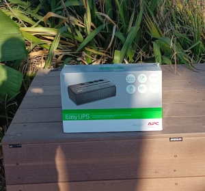 Déballage de l’onduleur APC Easy UPS 1000VA Boîte de l’onduleur APC Easy UPS posée sur un coffre en bois dans un espace vert
