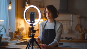 YouTubeuse cuisine enregistrant un podcast avec smartphone et anneau lumineux Créatrice culinaire qui enregistre un podcast avec un smartphone et un anneau lumineux pour l’éclairage